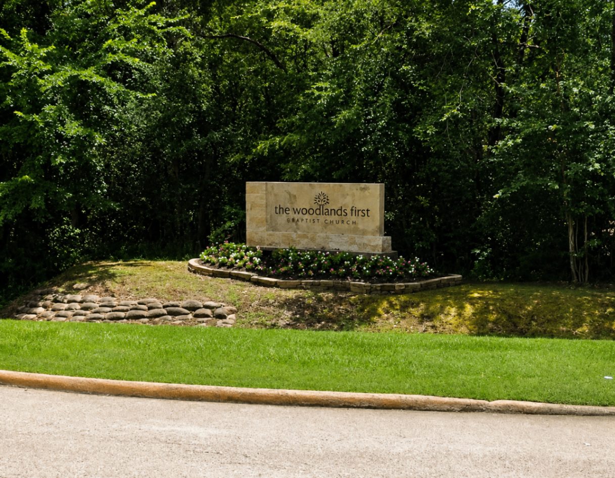 The Woodlands First Baptist Church sign in a wooded setting